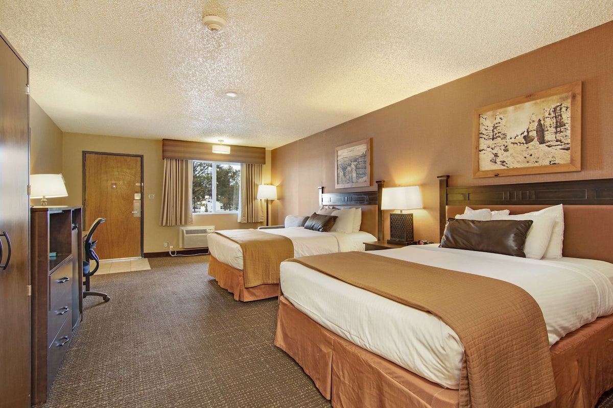 A hotel room with two beds, a desk, a dresser, and a window with curtains.