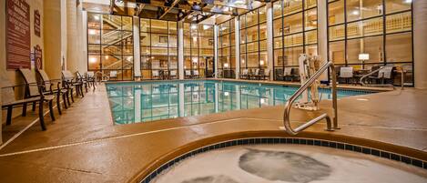 An indoor swimming pool with clear water, a hot tub, and lounge chairs.