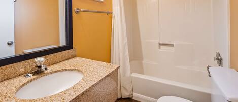 A bathroom with a granite countertop sink, a mirror, a white toilet, and a bathtub.