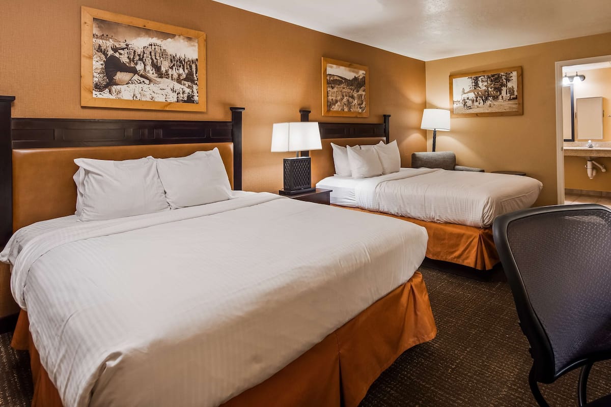 A hotel room with two beds, a desk, a chair, and a bathroom visible through an open door.