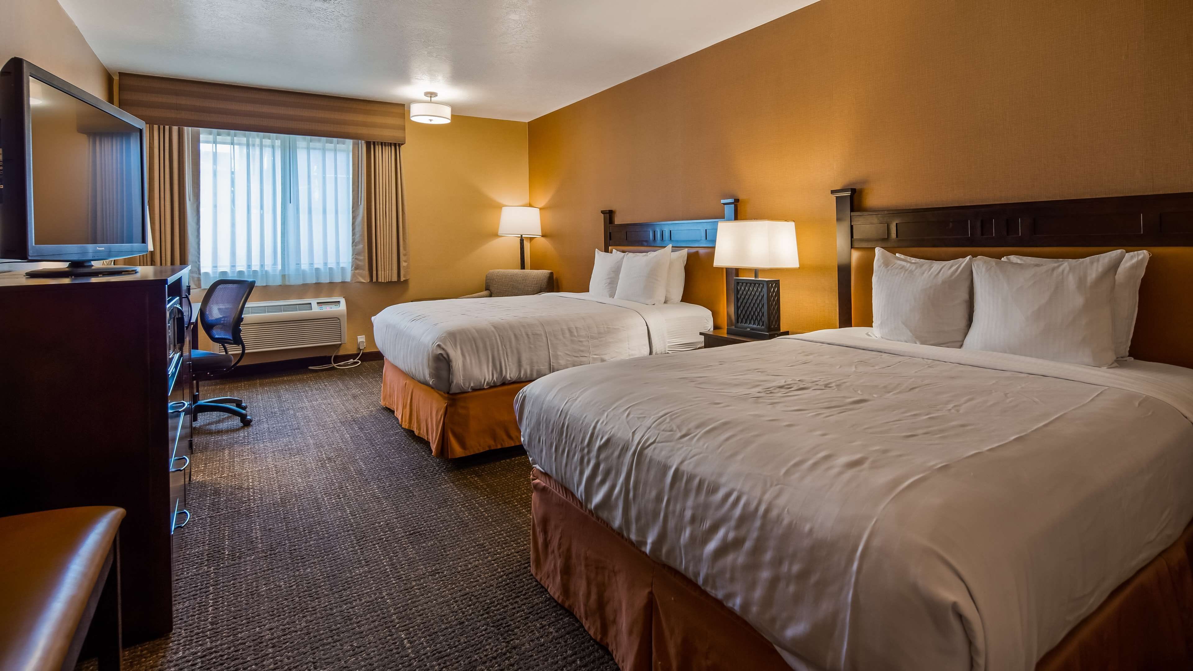 Une chambre d’hôtel avec deux lits, un bureau avec un ordinateur, une chaise et un téléviseur.