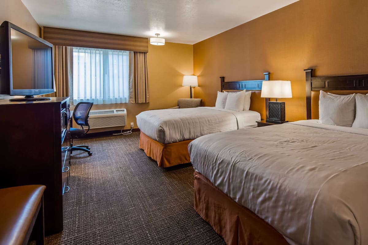 A hotel room with two beds, a desk with a computer, a chair, and a TV.