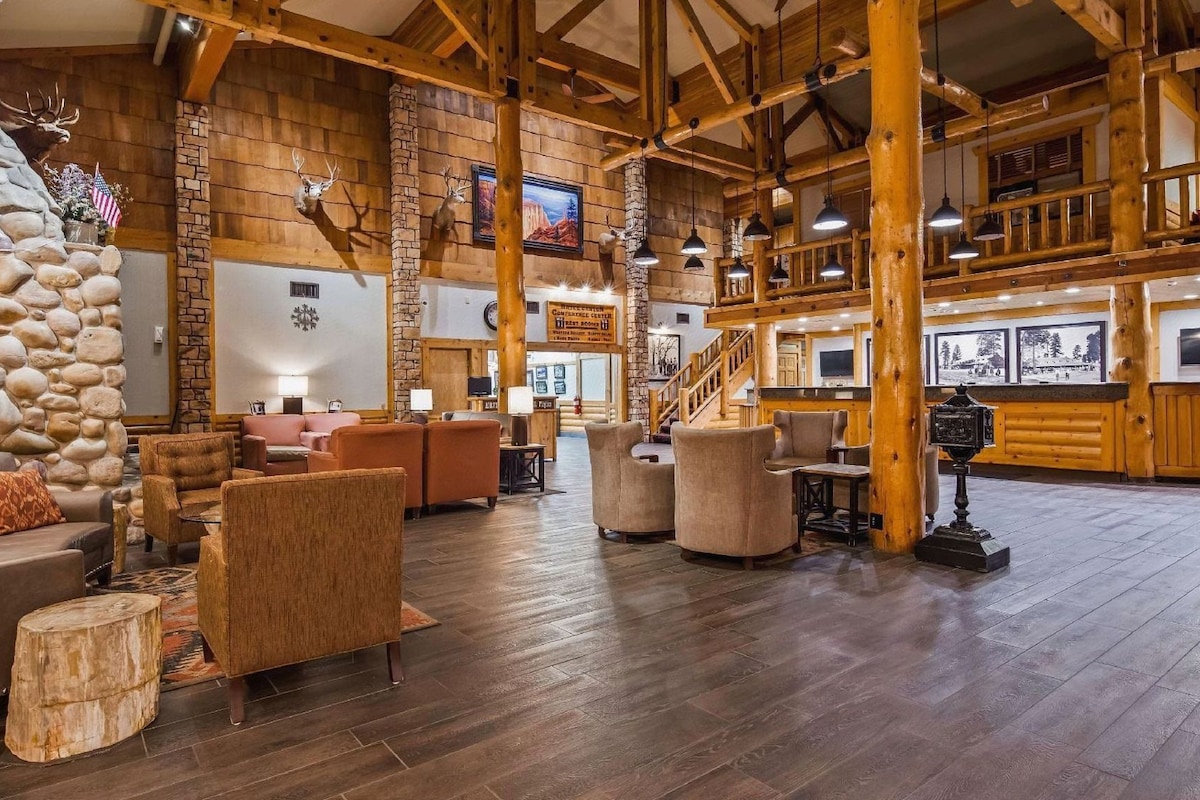 A spacious lobby with wooden beams, stone walls, and a stone fireplace. There are several seating areas with sofas and chairs.