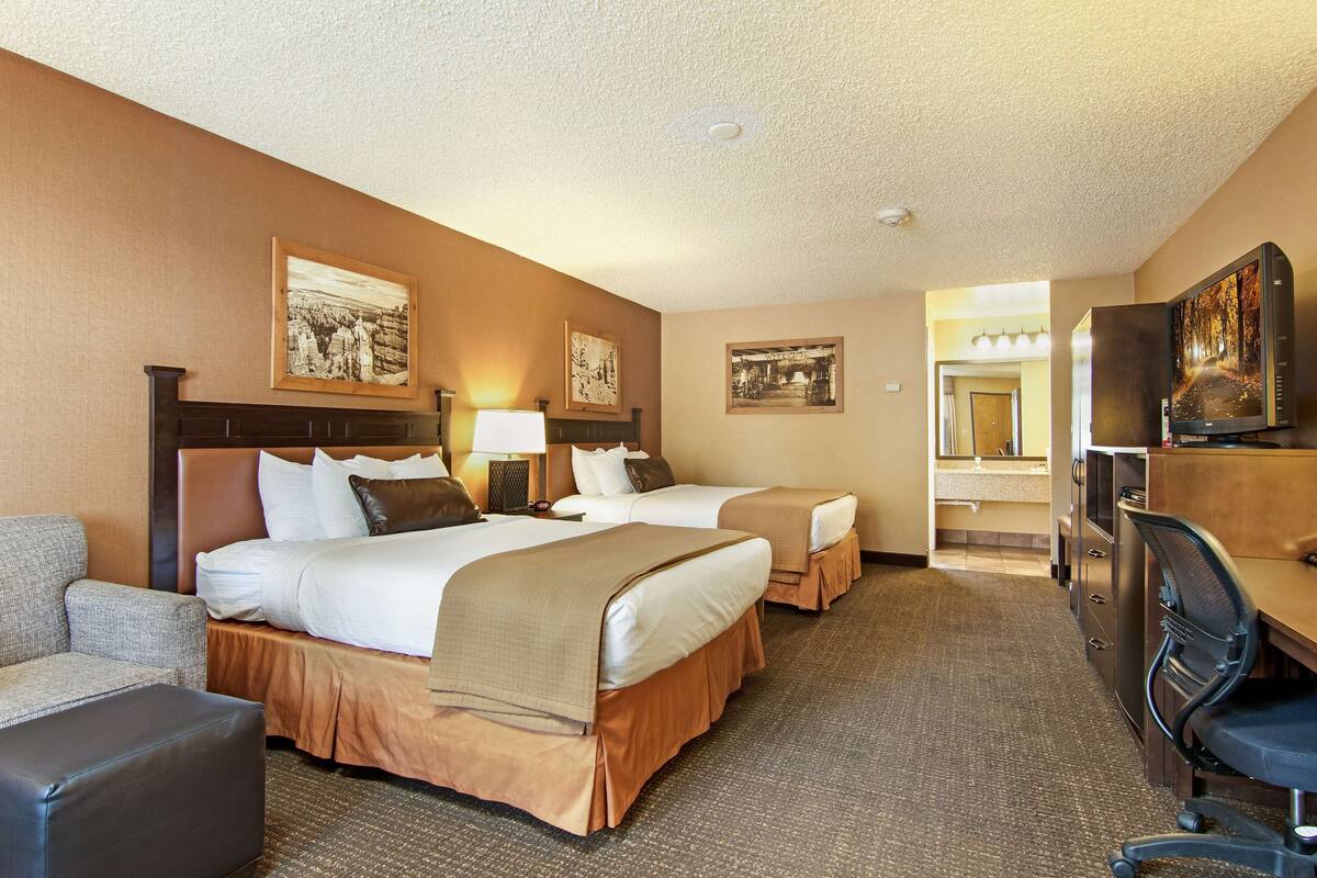 A hotel room with two beds, a desk, a chair, and a television.