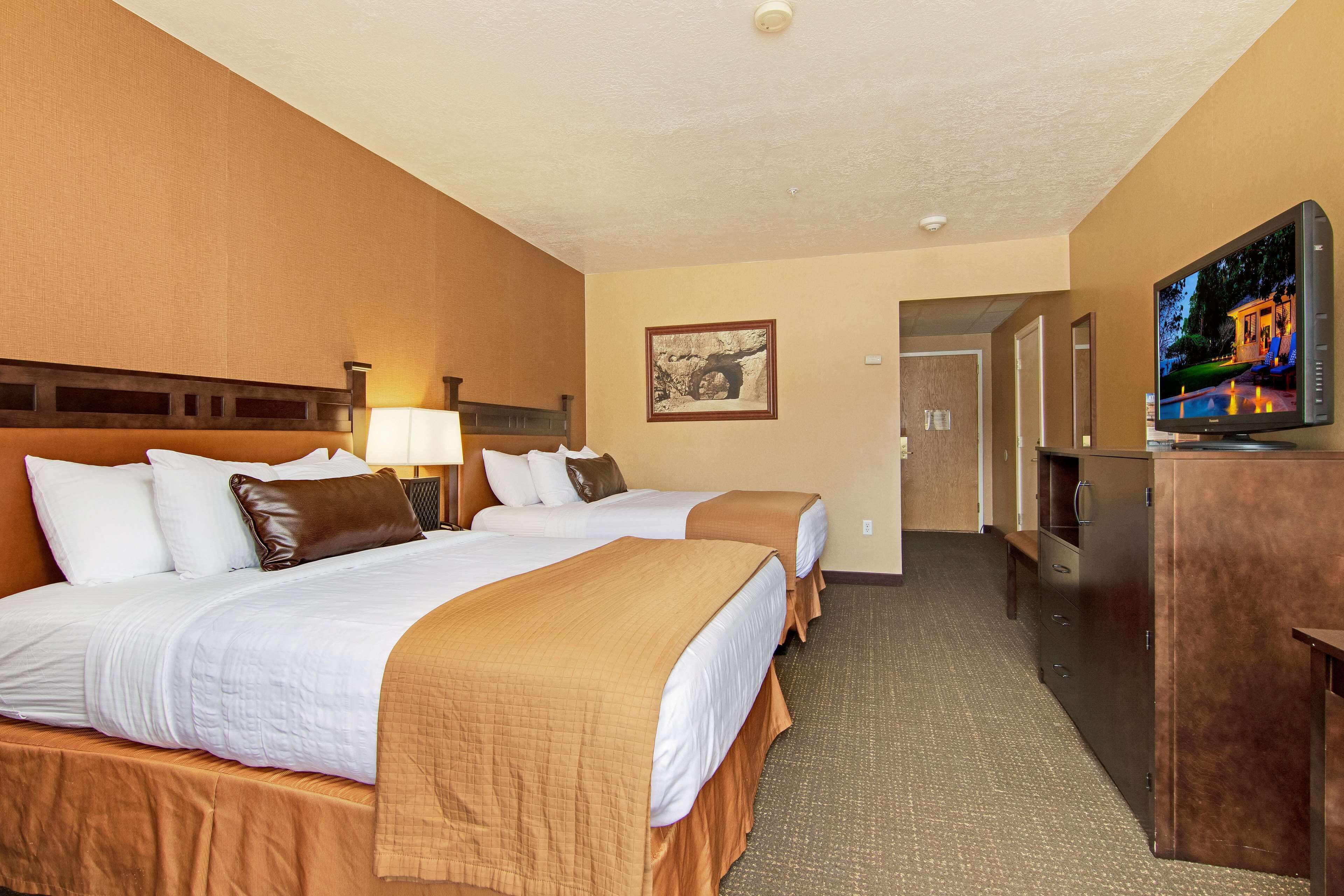 A hotel room with two beds, a TV, a desk, and a framed picture on the wall.