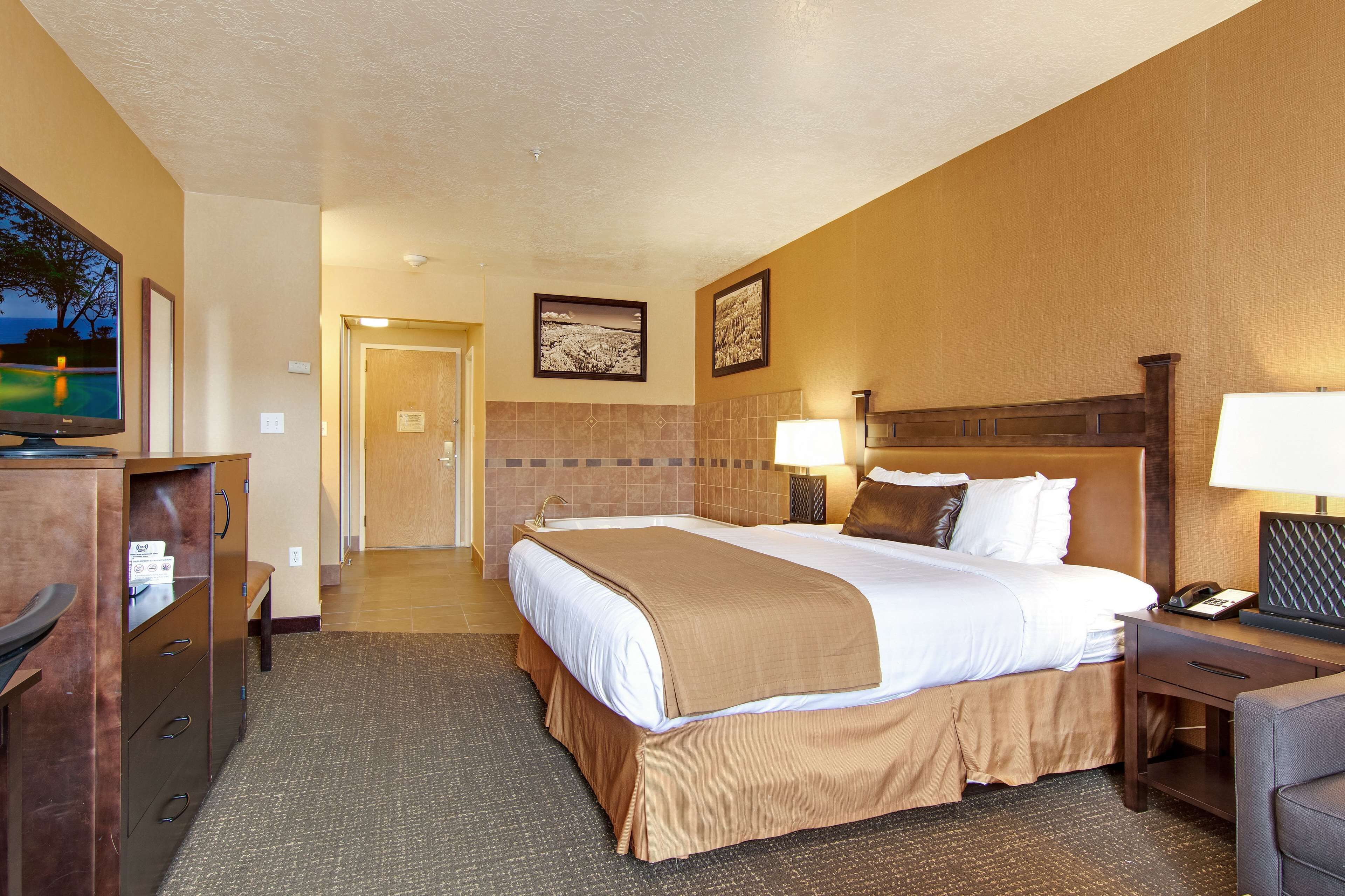 A hotel room with a large bed, a desk with a lamp, a television, and a door leading to another room.