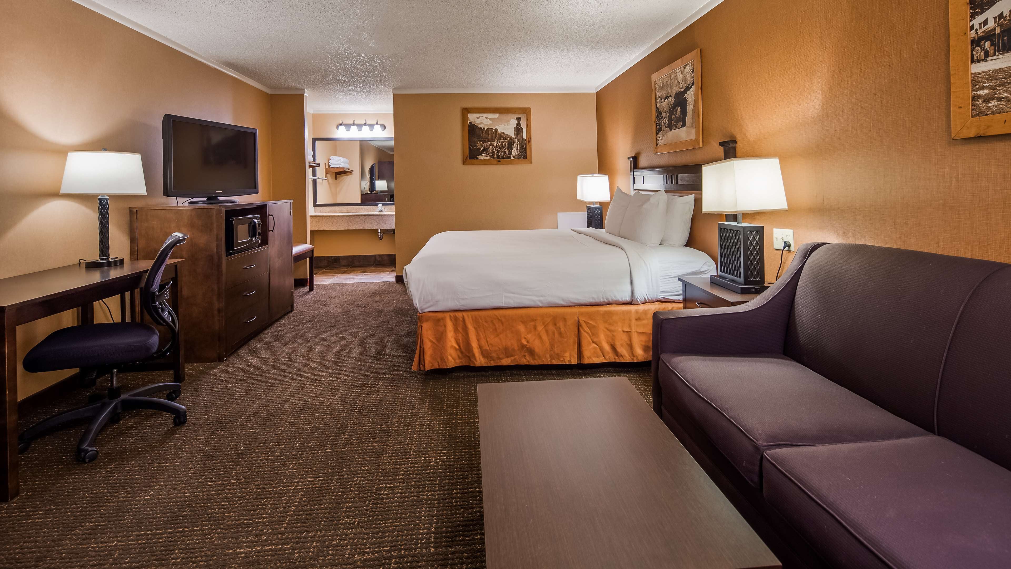 A hotel room with a bed, a desk with a chair, a television, a sofa, and a small table.