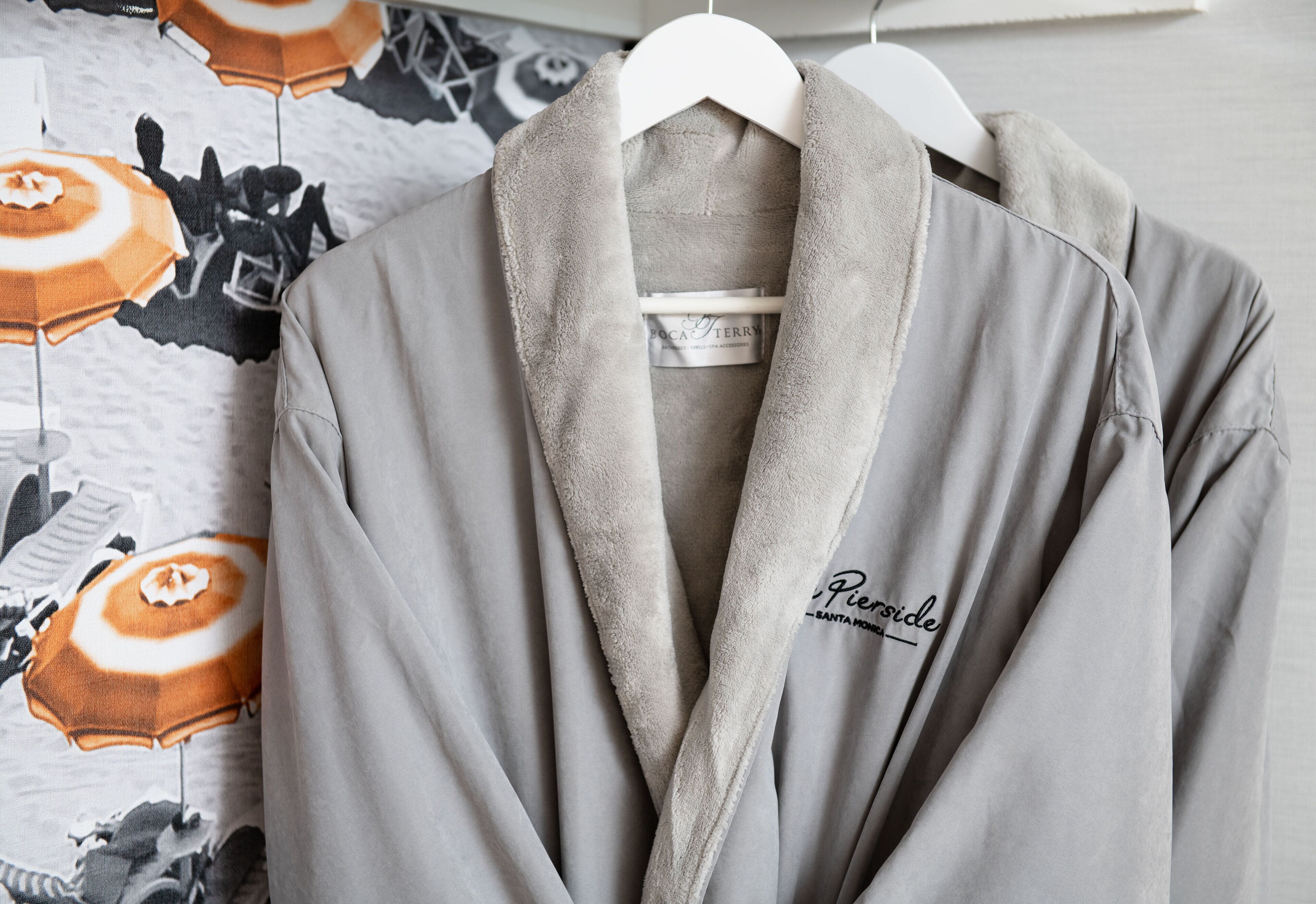 A grey robe with a fluffy collar and the text "Pier 13" on it, hanging on a white hanger.