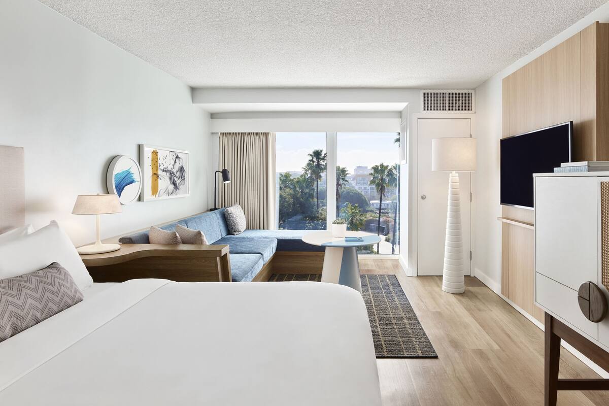 A modern hotel room with a large bed, a sofa, a dining table, and a TV.