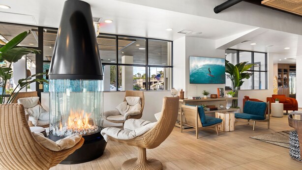 A modern lounge area with a central fire feature, comfortable seating, and large windows offering views of the outdoors.