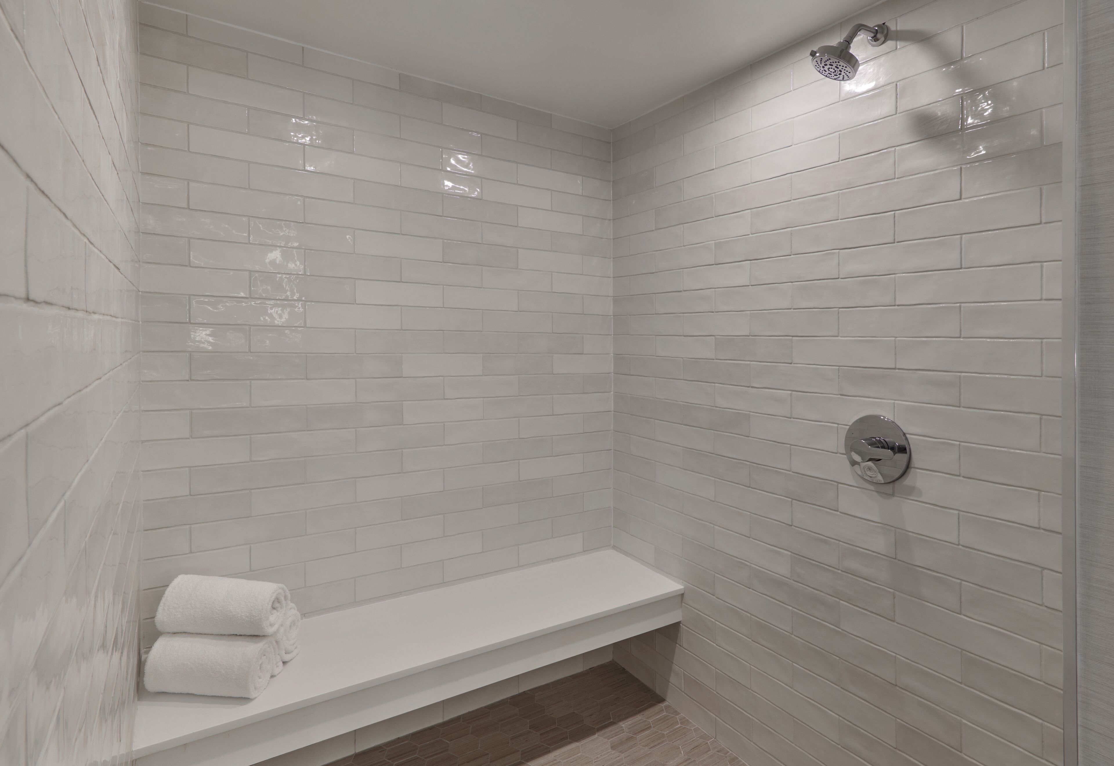 A modern shower with white tiles, a built-in bench, and a handheld showerhead.