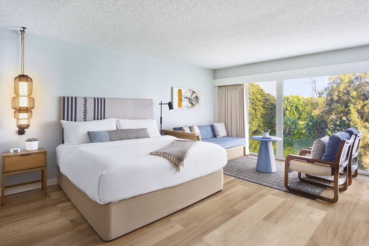 A modern hotel room with a large bed, a seating area, and a view of the outdoors.