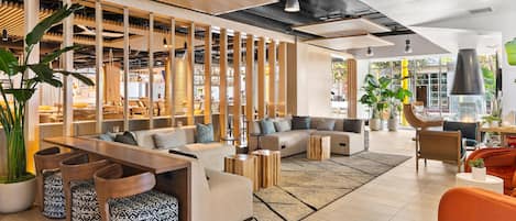 Un área de estar moderna con un separador de madera, disposición de asientos y una planta grande en maceta.