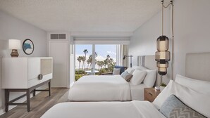 A hotel room with two beds, a desk, and a view of palm trees.
