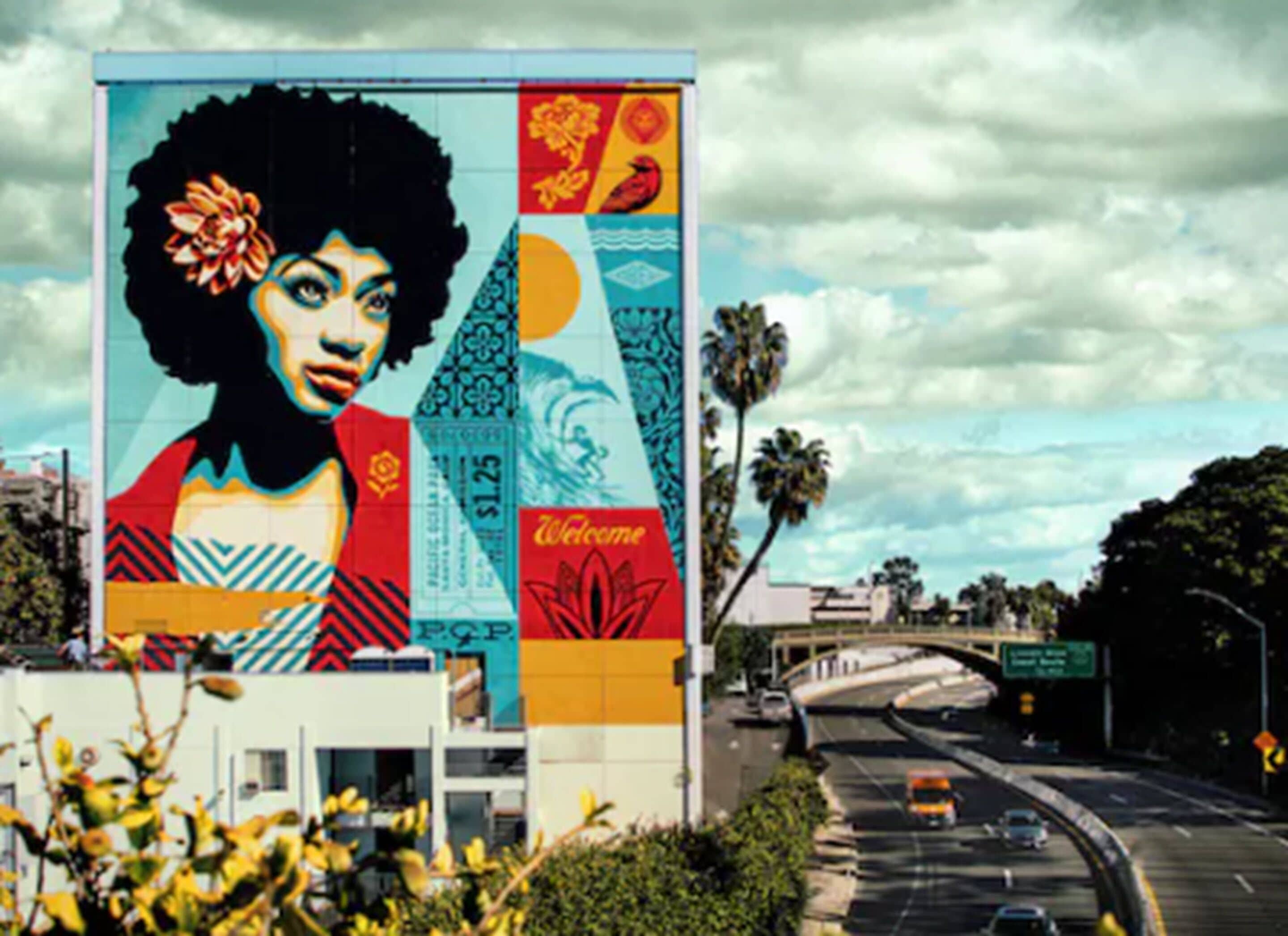 Um grande mural numa fachada com padrões geométricos e um letreiro chamativo com a palavra 'Welcome'.