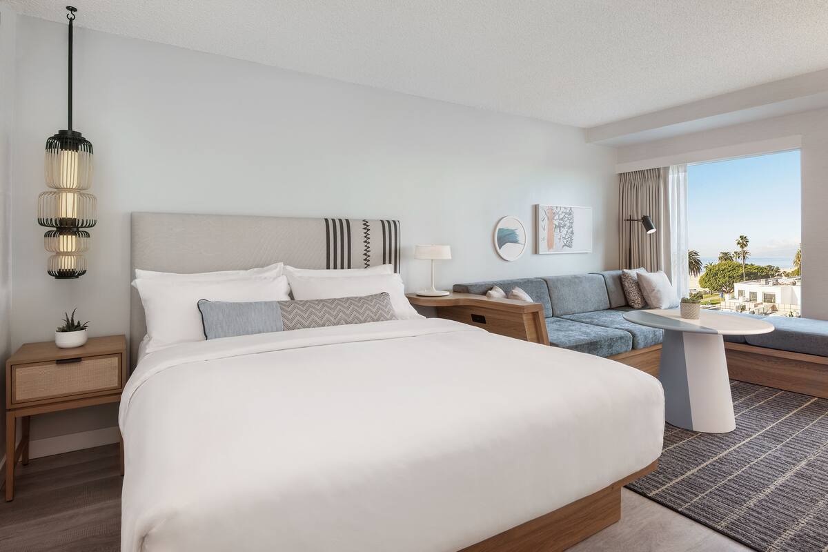 A modern hotel room with a large bed, a sofa, a small table, and a view of the city.