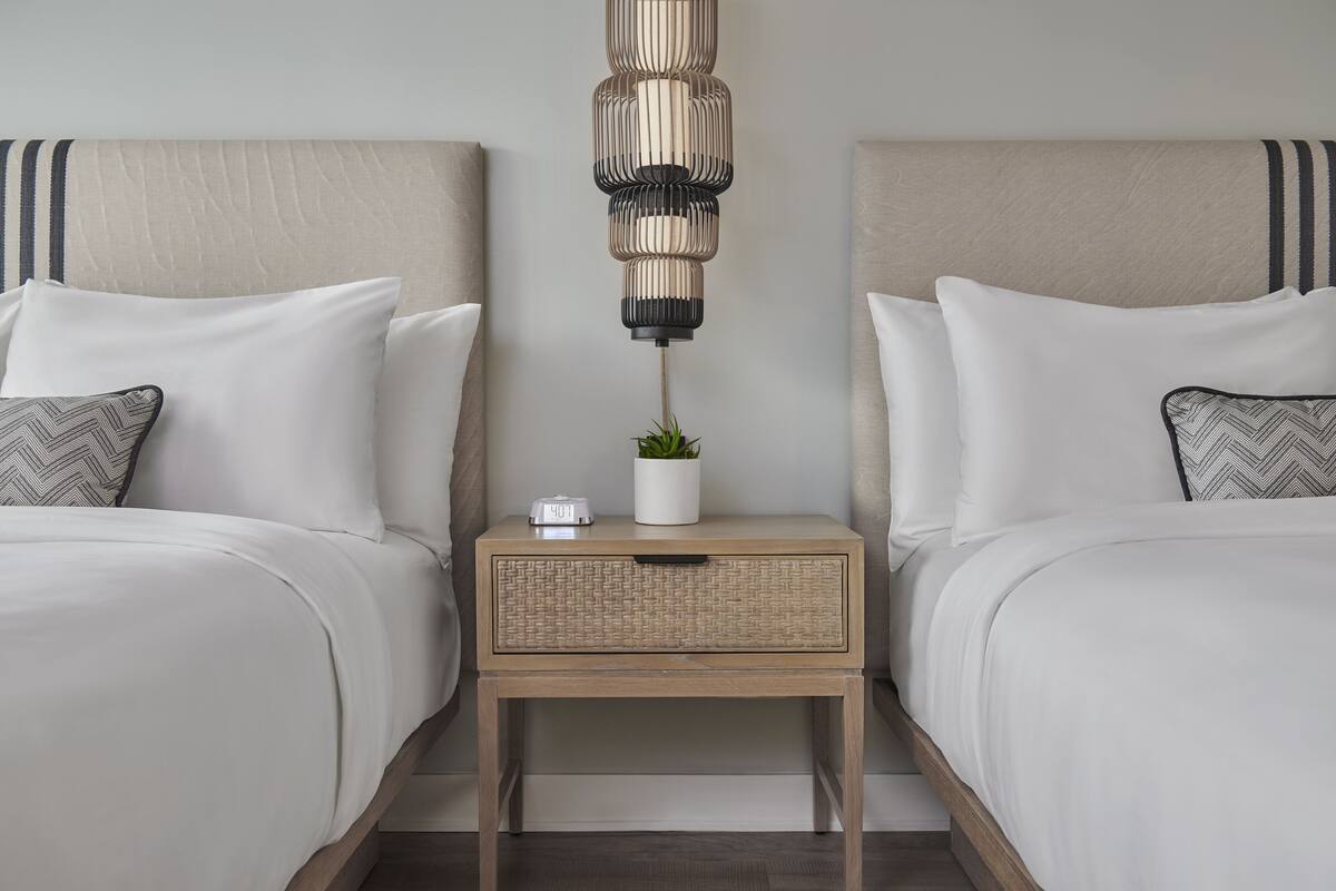 A double bed with a wooden nightstand in between, a small potted plant, and a white bedside table lamp.