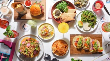 Verschiedene Speisen und Getränke auf einem Tisch, darunter Tacos, ein Burger und ein Salat.