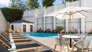 A poolside area with sun loungers, a table with chairs, and a white umbrella.