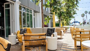 An outdoor seating area with wicker furniture, a patterned rug, and a view of a building with large windows.