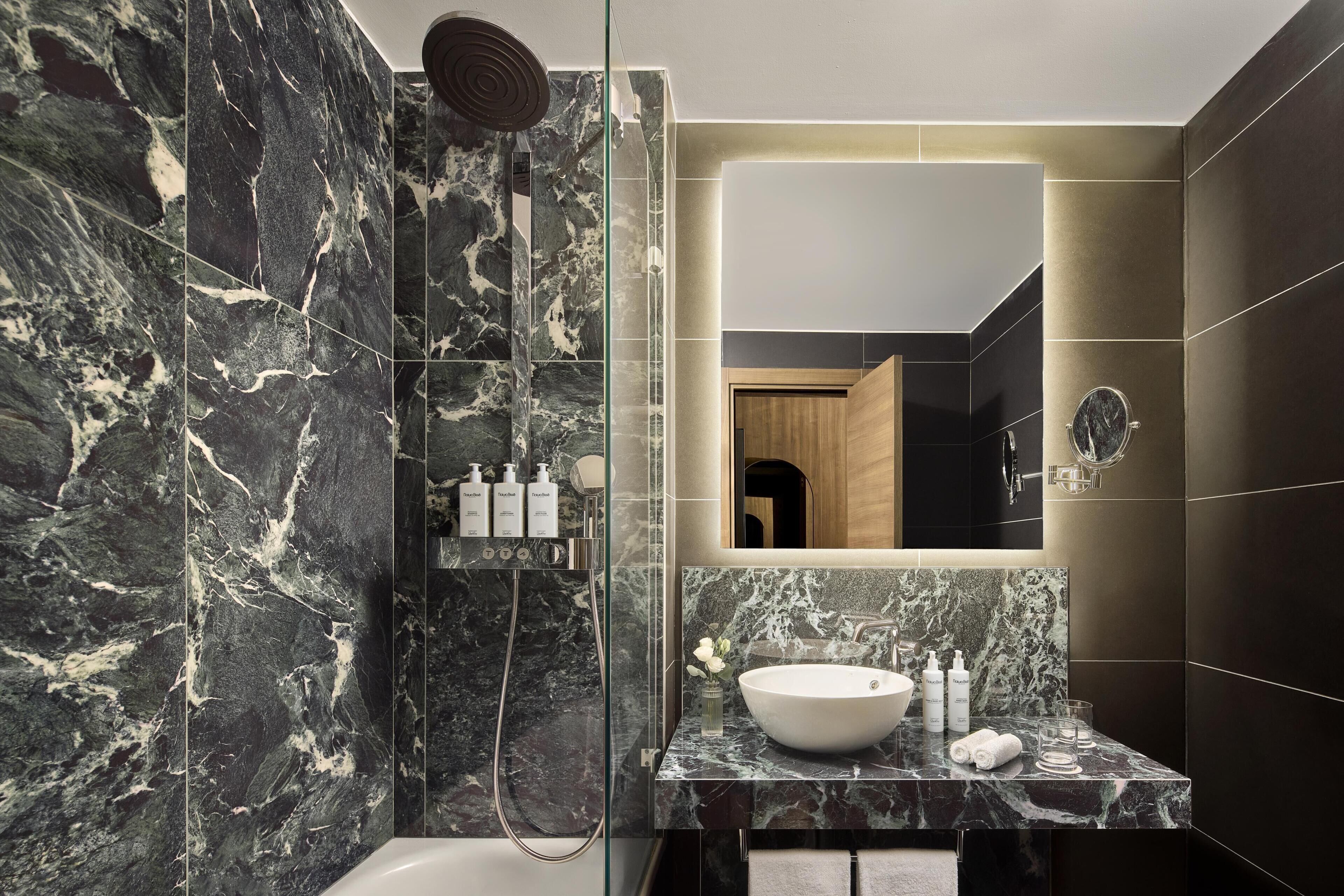 A modern bathroom with a marble shower, a large mirror, and a sink with toiletries.