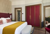 A hotel room with a large bed, a wardrobe, a mirror, and a seating area.