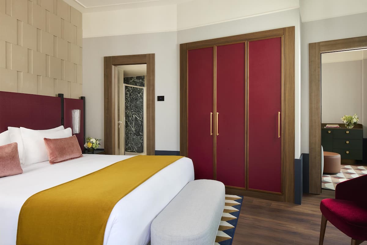 A hotel room with a large bed, a wardrobe, a mirror, and a seating area.