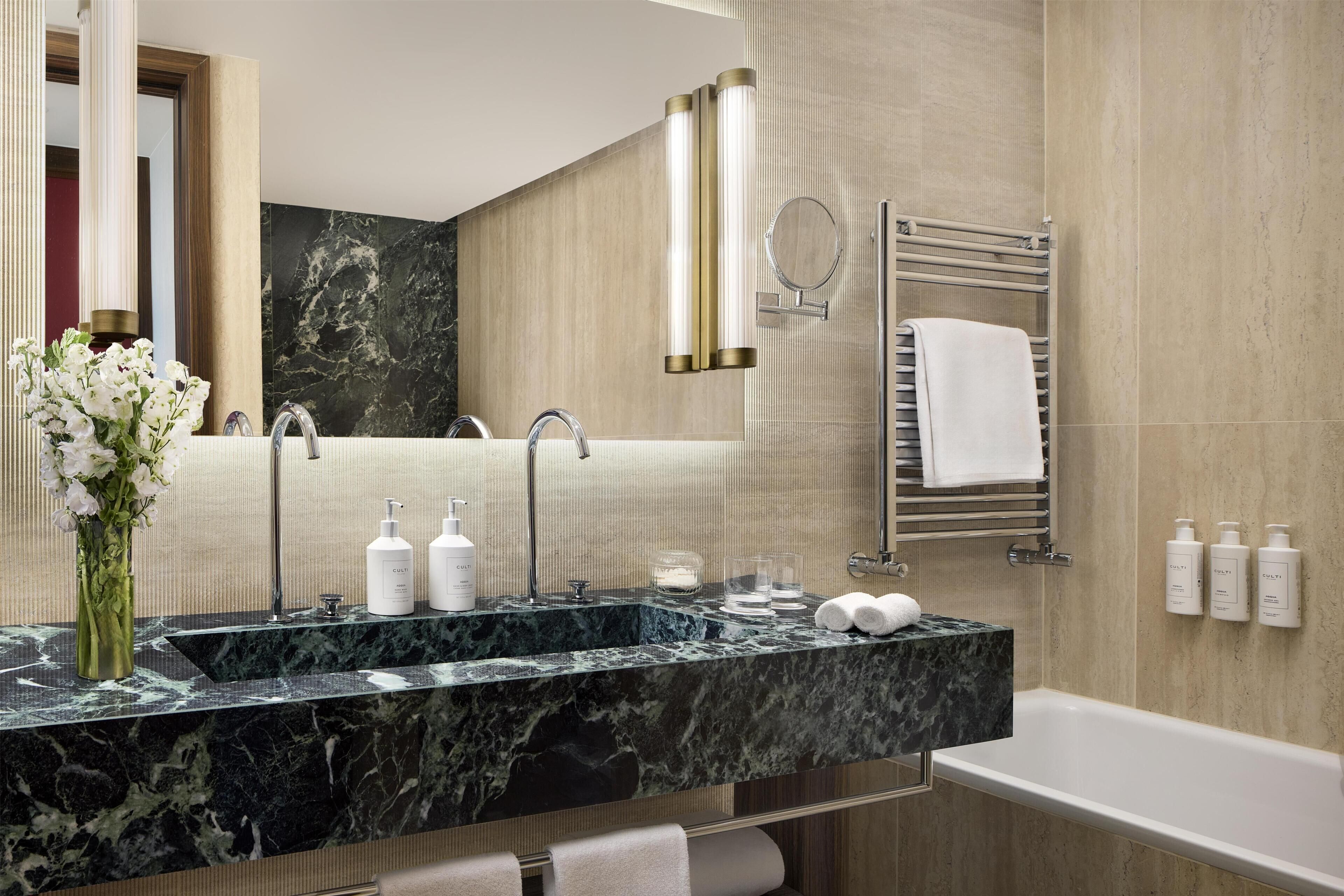 A bathroom with a marble sink, a mirror, a towel rack, and toiletries.