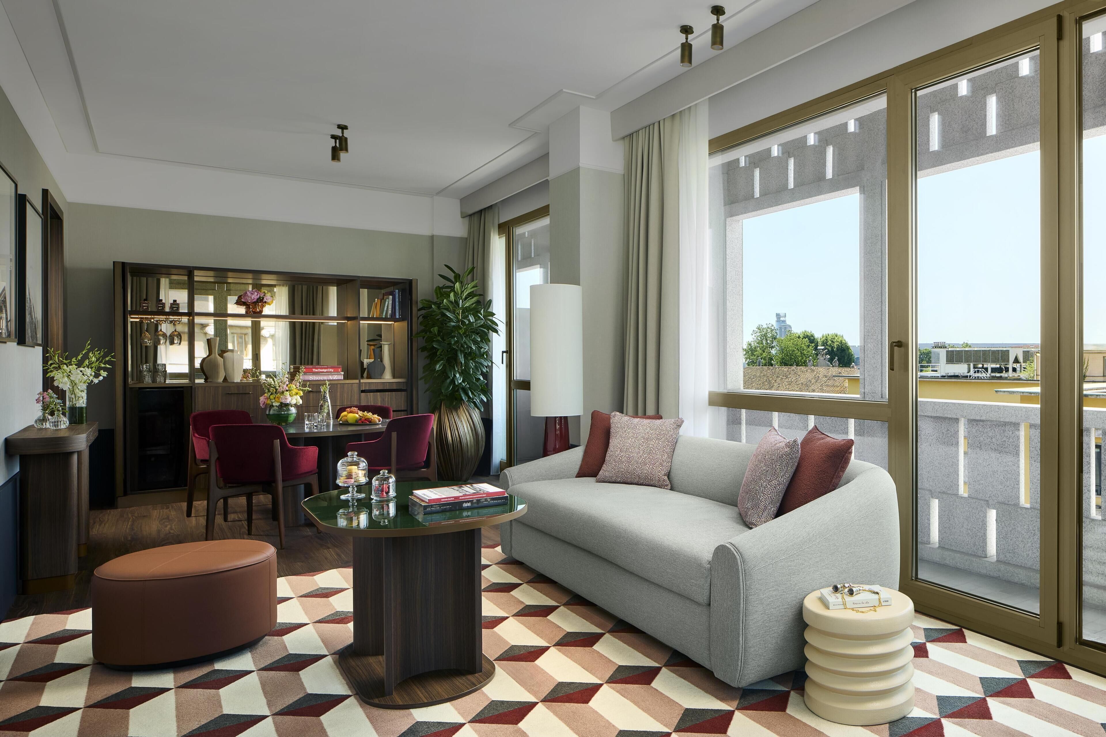 A modern living room with a sofa, coffee table, and a dining area with chairs and a bookshelf.