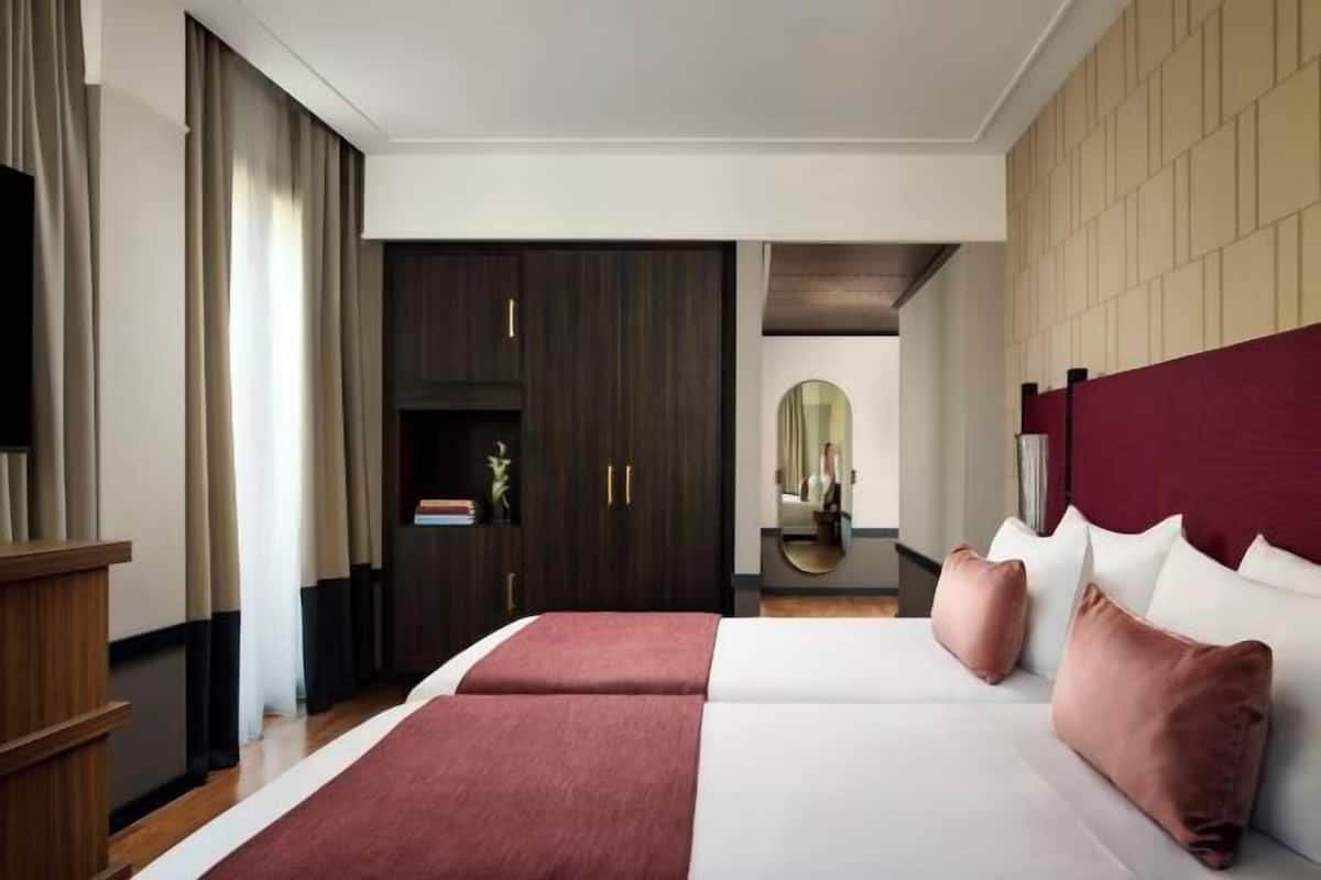 A hotel room with a large bed, a wardrobe, a mirror, and a red accent wall.
