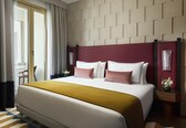 A hotel room with a large bed, a wooden headboard, a small table with a vase of flowers, and a window with curtains.