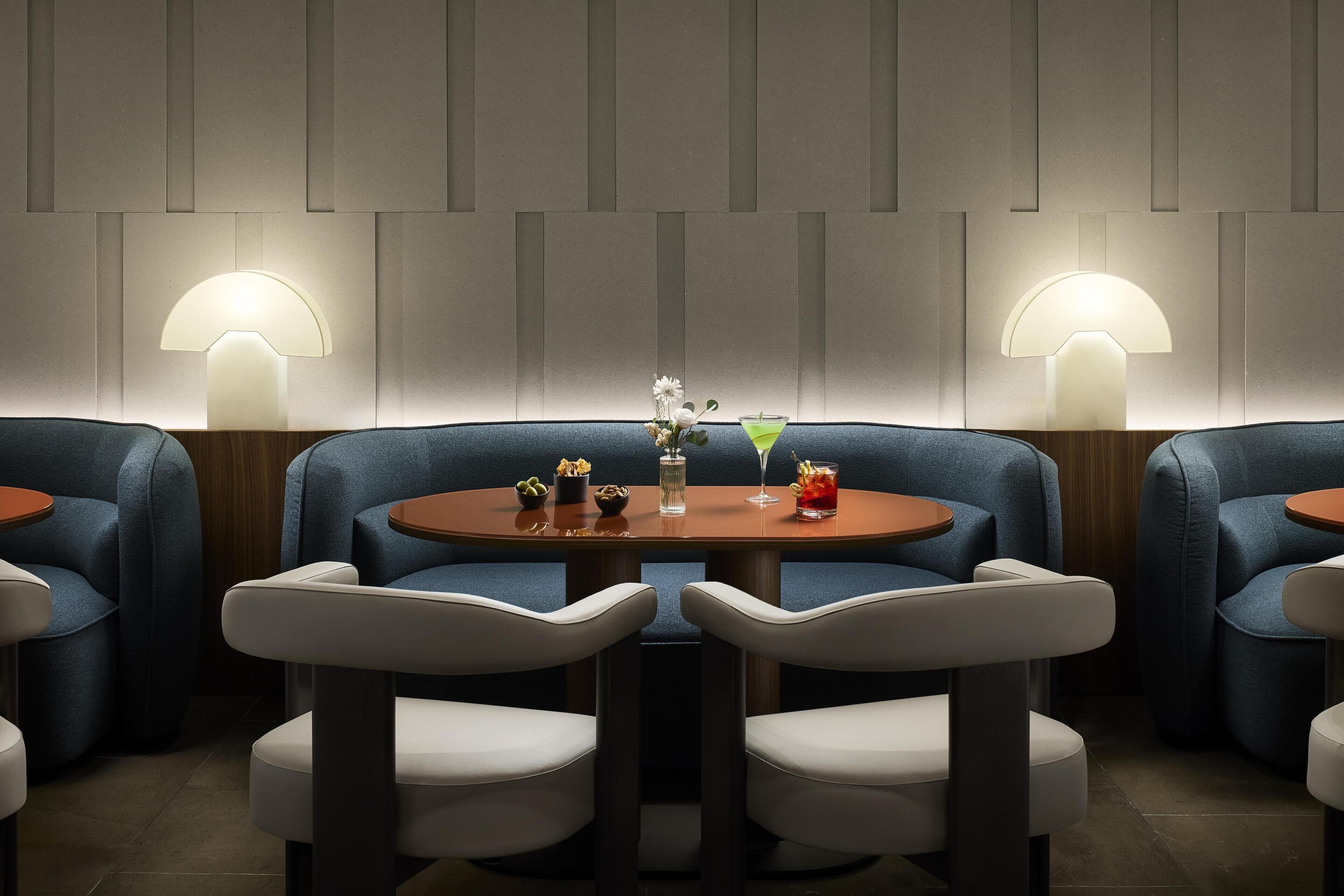 Un restaurant avec des tables rondes, des chaises recouvertes de tissu bleu et des lampes fixées au mur.