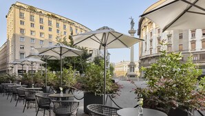 Outdoor seating with umbrellas, potted plants, and a statue in the background.