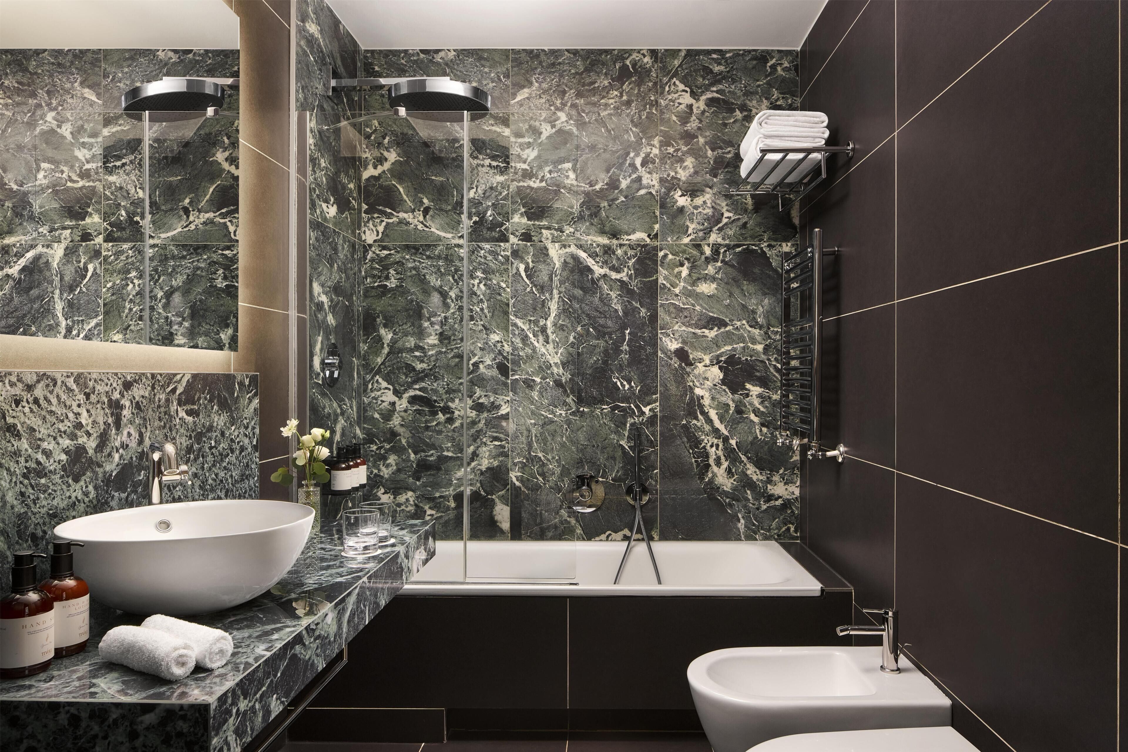 A modern bathroom with a large oval sink, a bathtub, a separate pedestal sink, and a vanity with a mirror.