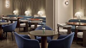 A modern lounge area with round tables, blue upholstered chairs, and ambient lighting.