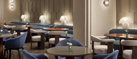 A modern lounge area with round tables, blue upholstered chairs, and ambient lighting.
