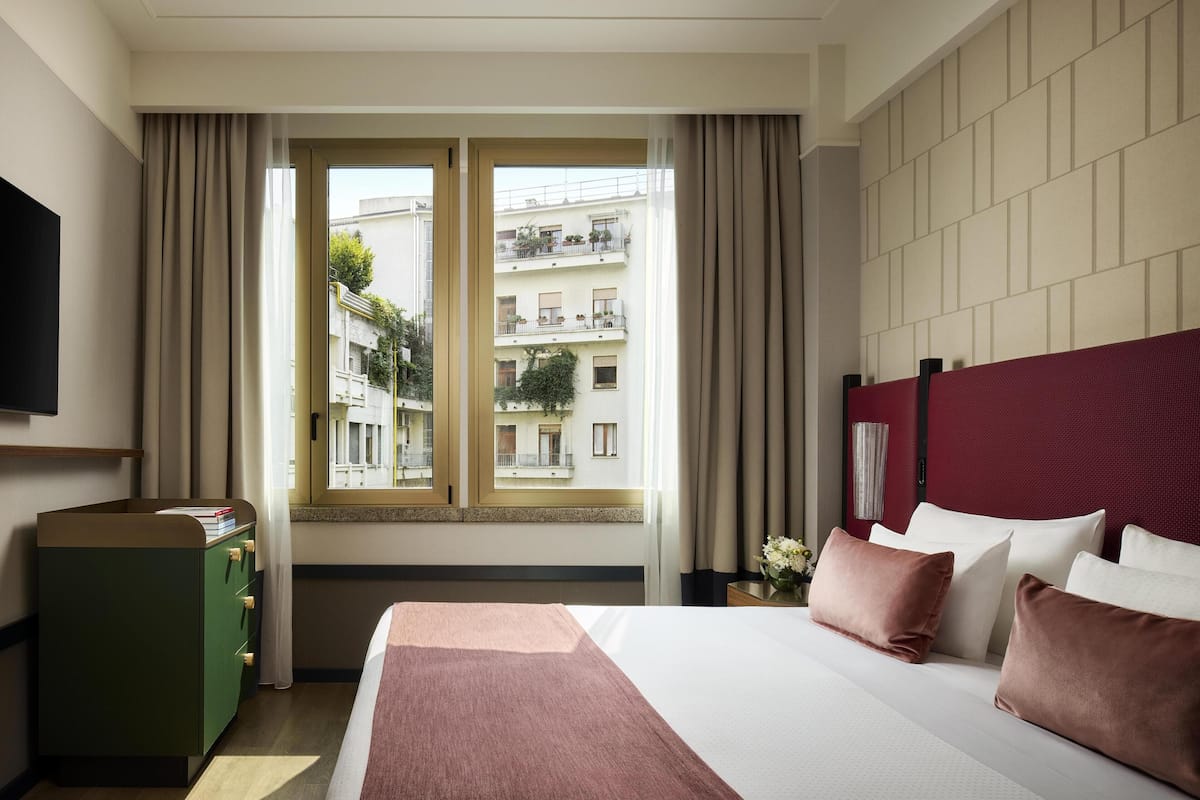 A hotel room with a bed, a green dresser, a TV, and a window with curtains.