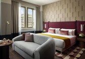 A hotel room with a bed, a sofa, a nightstand, a lamp, and a window with curtains.