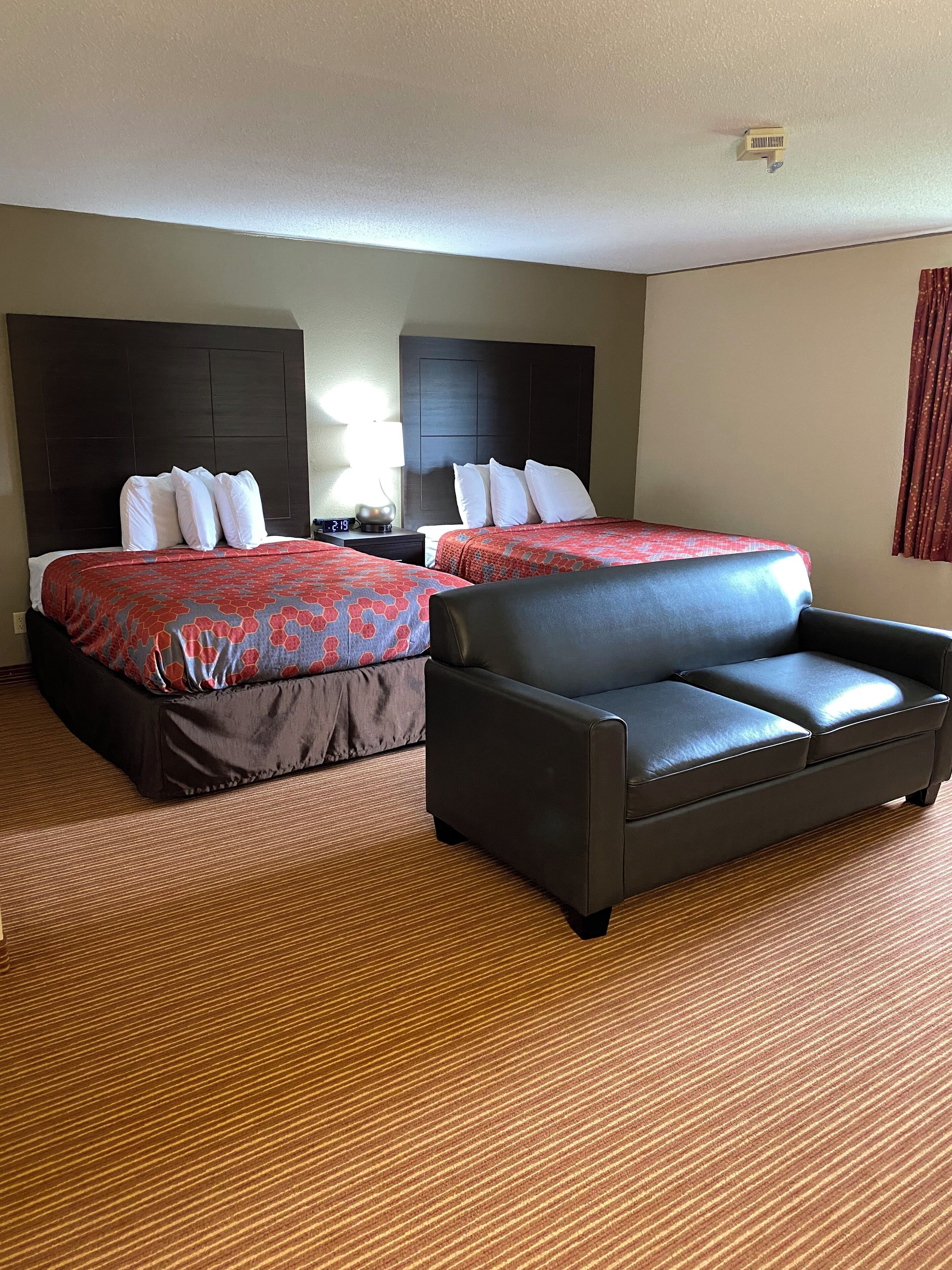 Une chambre d’hôtel avec deux lits, un canapé en cuir noir et un sol recouvert de moquette.