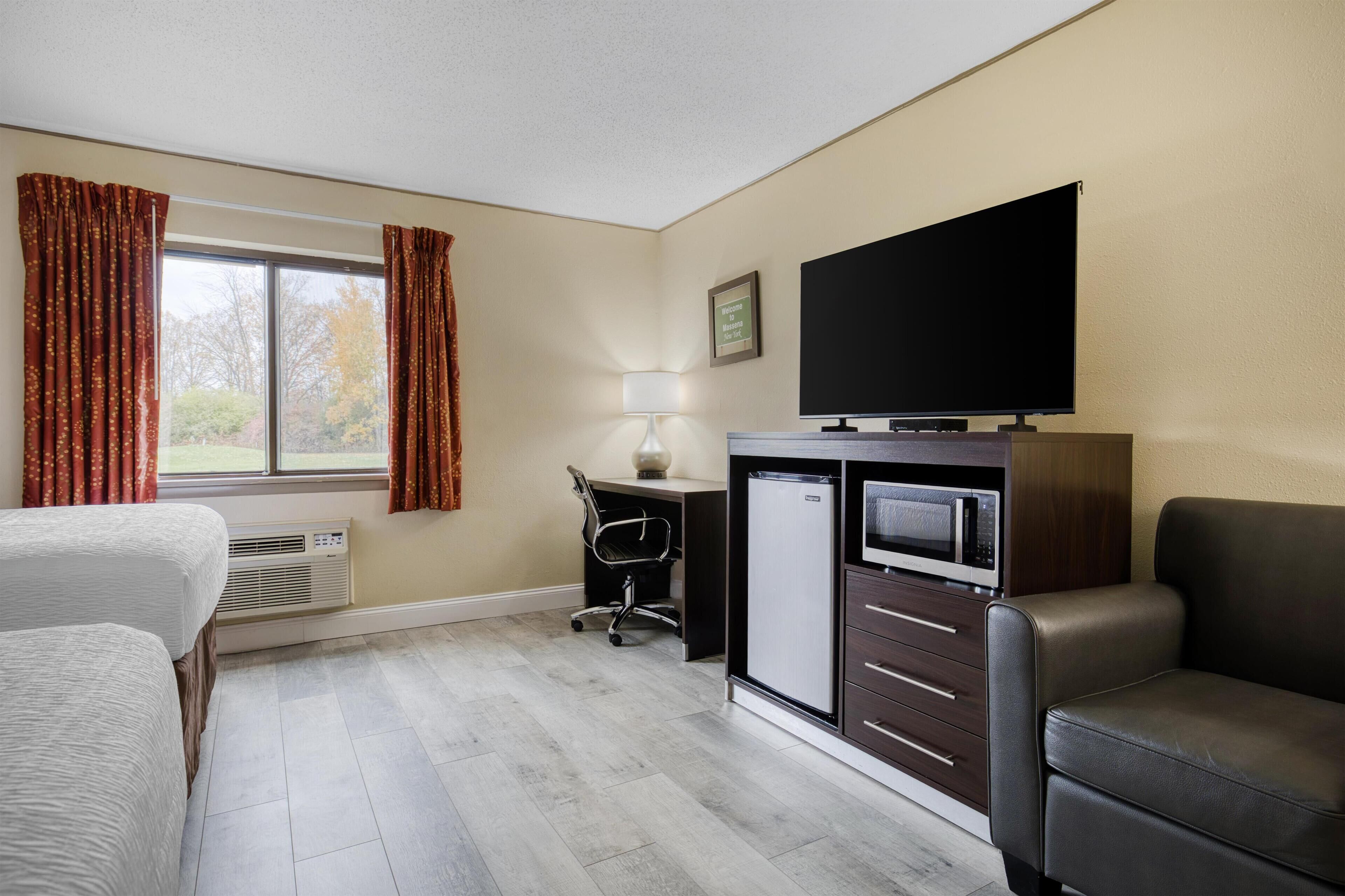 Una habitación de hotel con una cama, un escritorio con computadora, televisor y refrigerador.