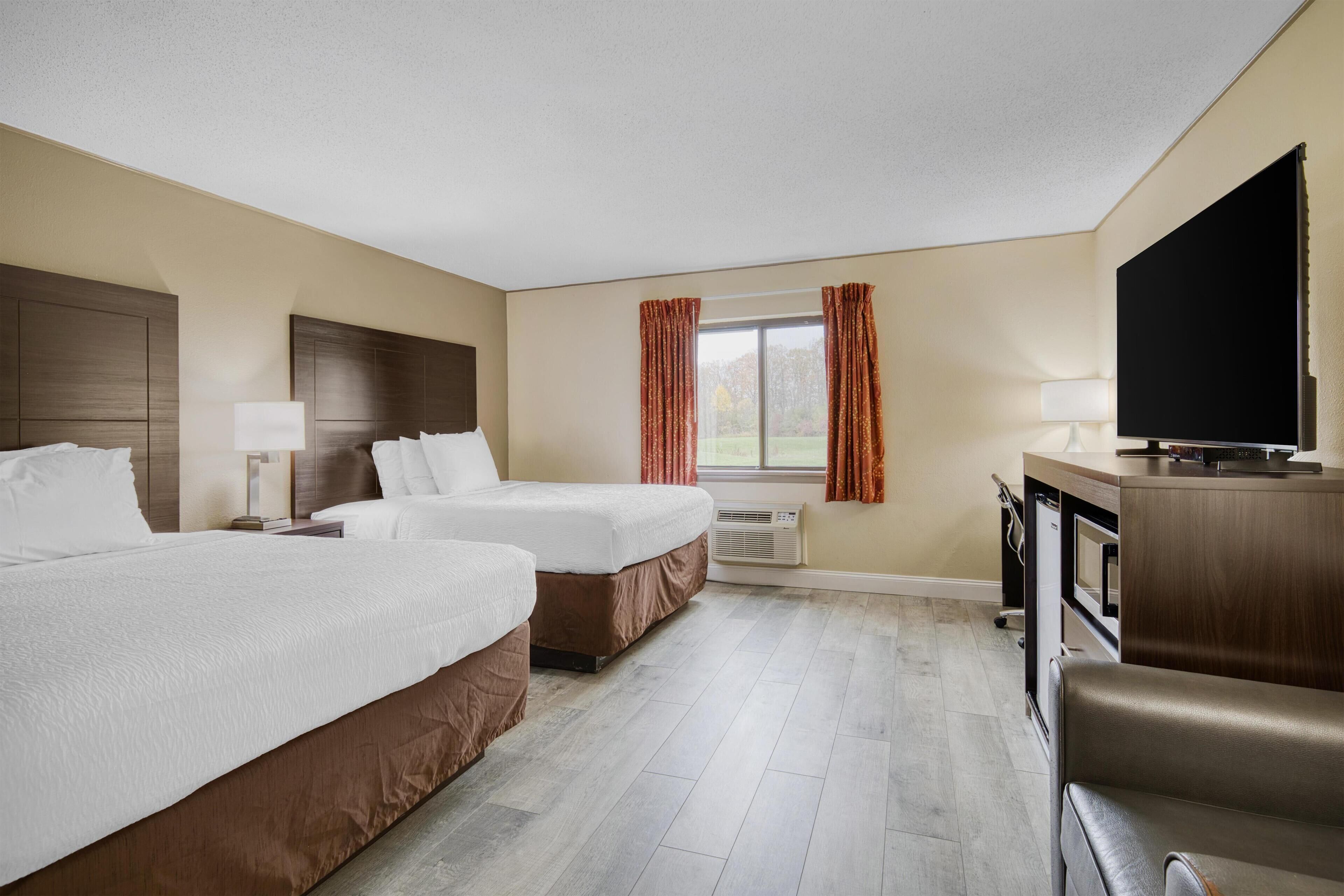 Habitación de hotel con dos camas, televisión, escritorio y ventana con cortinas.