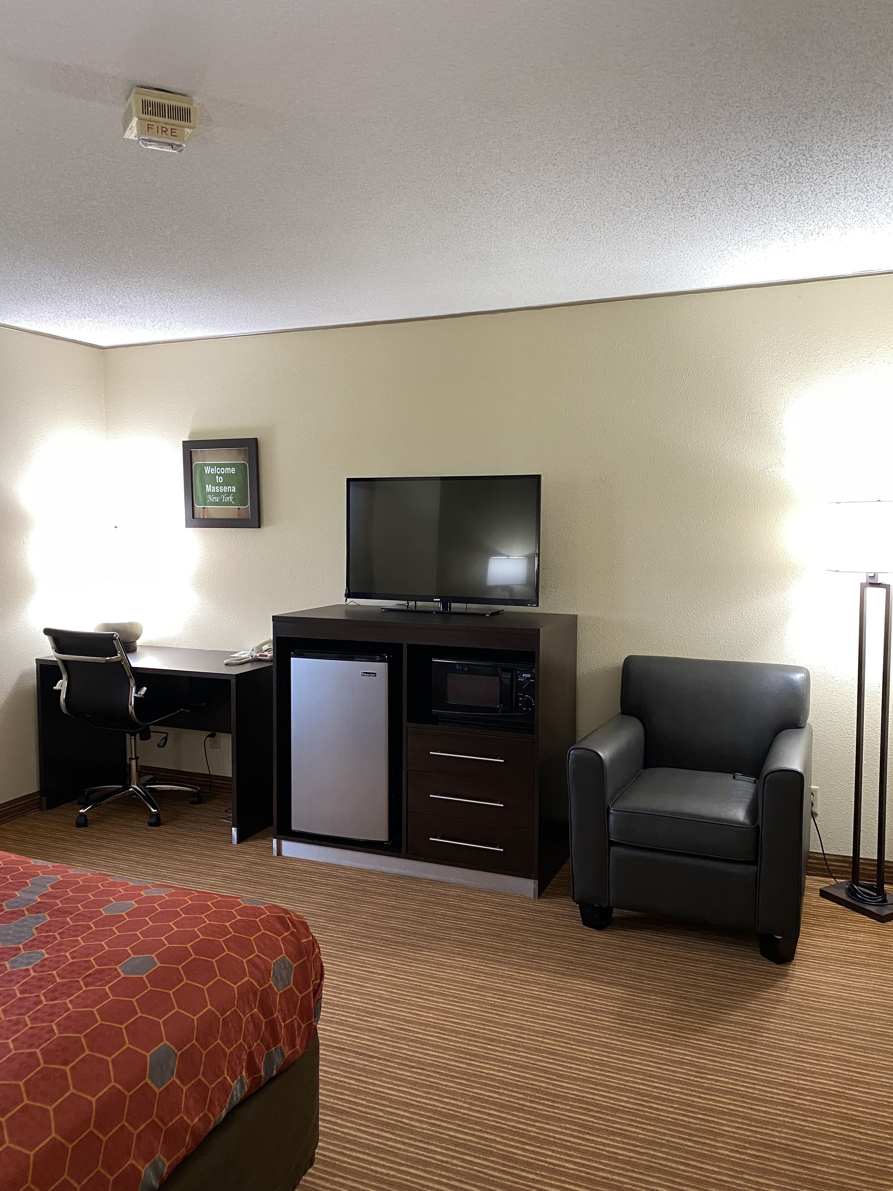 Habitación de hotel con cama, escritorio, silla, televisor y un refrigerador pequeño.