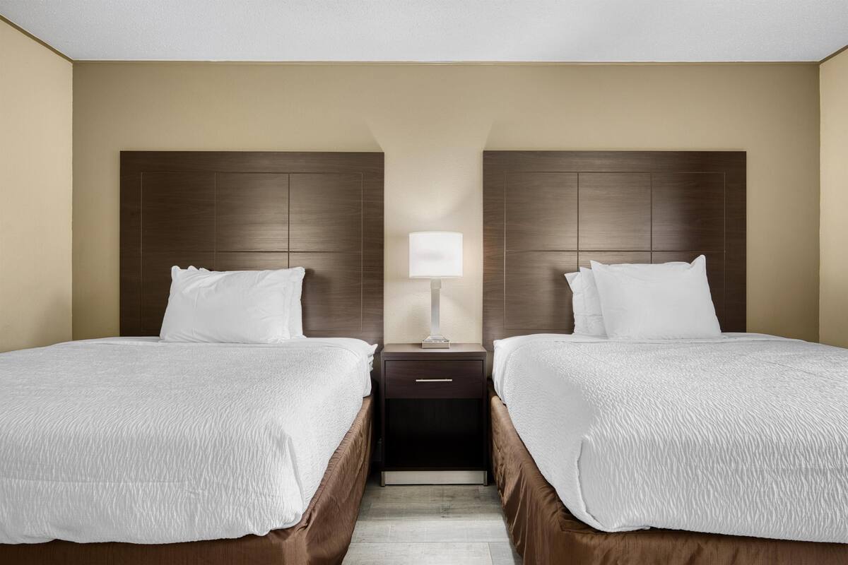 Een hotelkamer met twee bedden, een nachtkastje met een lamp en een houten hoofdeinde.
