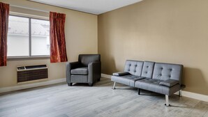 A living room with a grey sofa, a black armchair, and a window with red curtains.