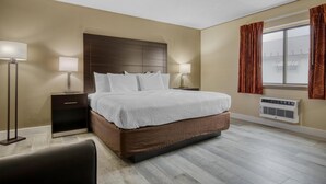 A hotel room with a large bed, two bedside tables with lamps, a window with curtains, and an air conditioning unit.