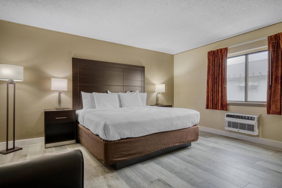 Een hotelkamer met een groot bed, twee nachtkastjes met lampen, een raam met gordijnen en een airconditioning.