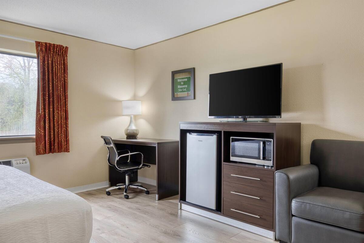 Een hotelkamer met een bed, bureau, stoel, koelkast, magnetron, televisie en een bank.