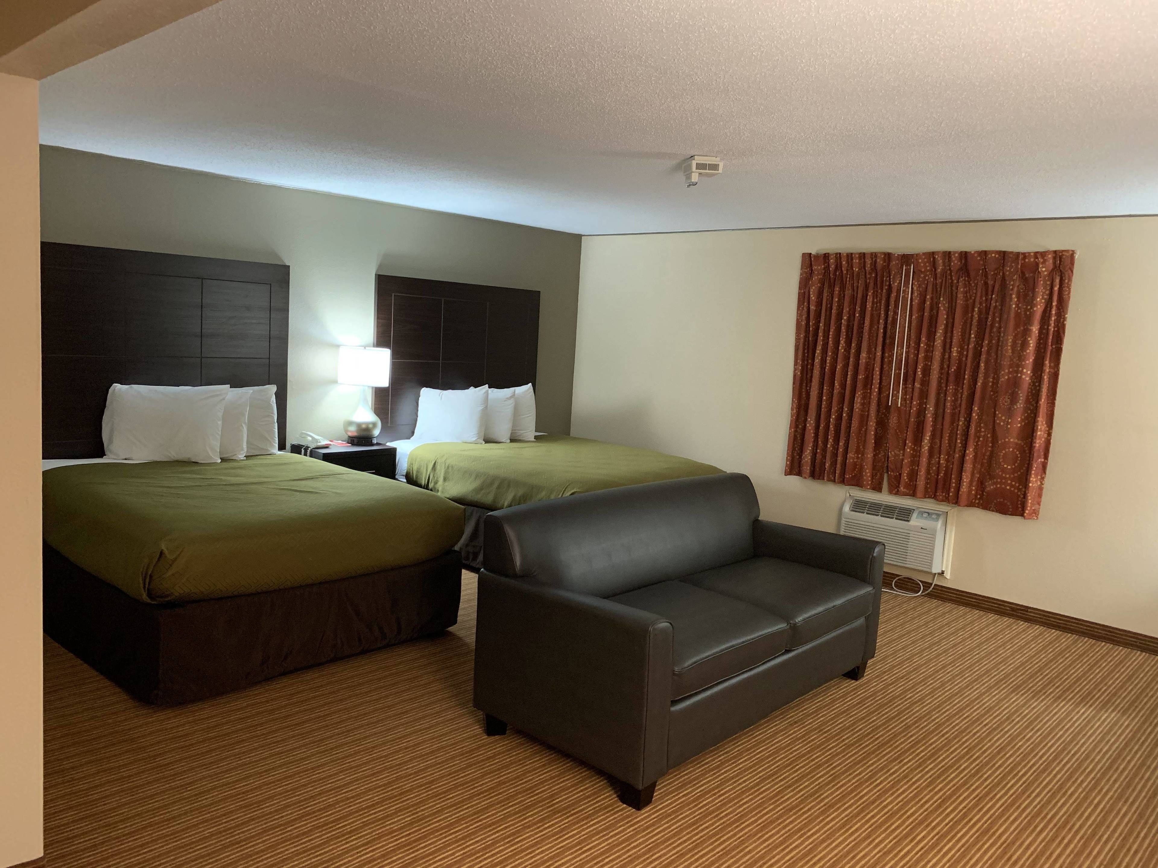 Una habitación de hotel con dos camas, un sofá, una mesita de noche con lámpara y una ventana con cortinas.