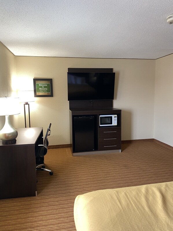 Habitación de hotel con televisión de pantalla plana, mini refrigerador, microondas, escritorio con lámpara y una silla.