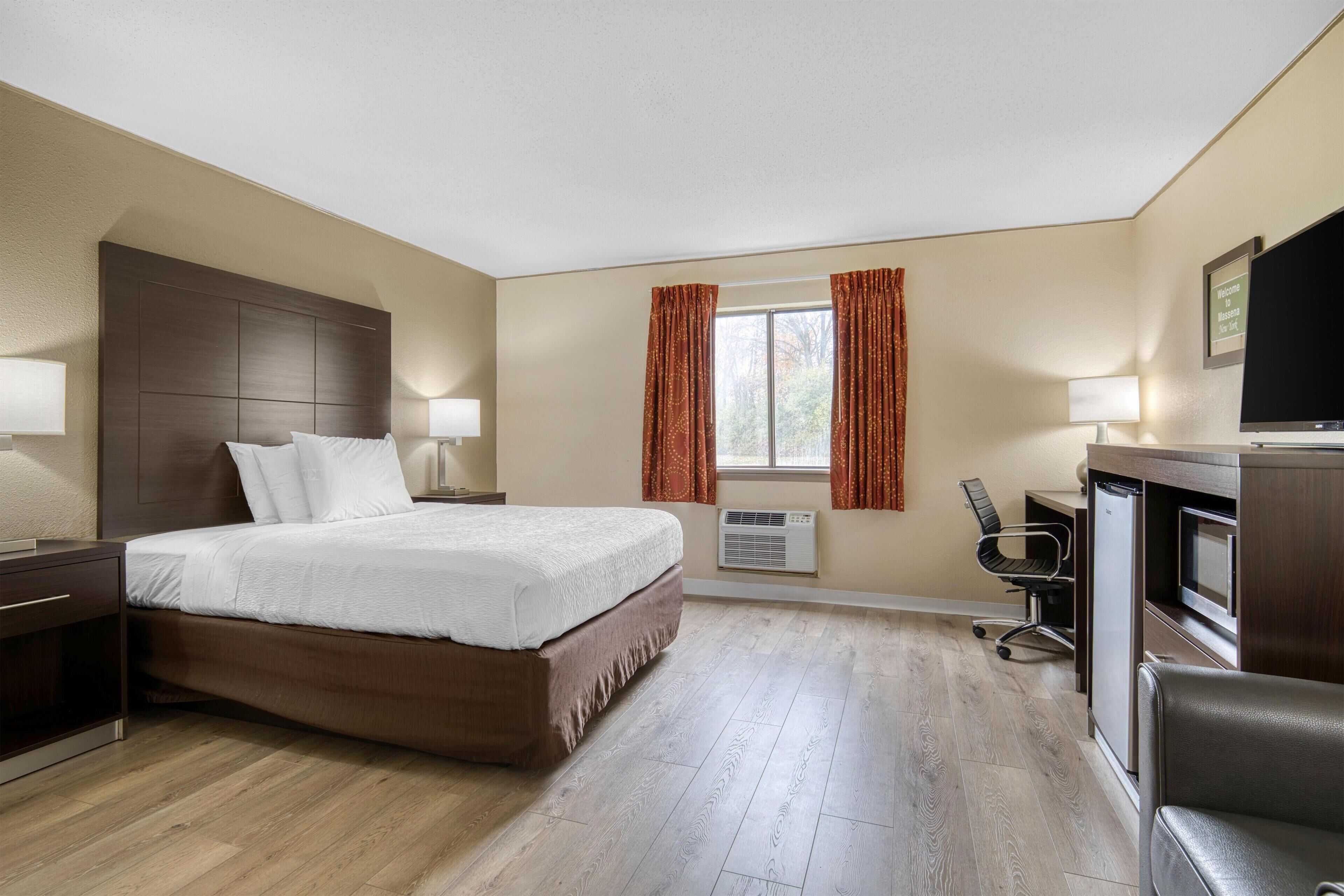 Habitación de hotel con una cama grande, un escritorio con computadora, televisión y aire acondicionado.